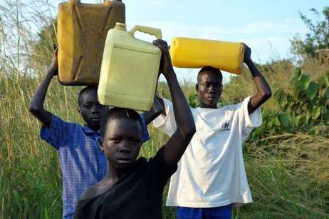 Denis Opoka (1er à droite) et son frère et sa soeur font la corvée d'eau au village Ajulu au nord de l'Ouganda (Xinhua/Tian Ye)